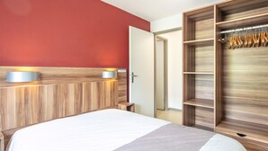 A hotel room with a bed, a wooden headboard, a red accent wall, and a wardrobe with a hanging rack. - Apartment in Gresse-en-vercors Near Ski-lift (Gresse-en-Vercors)
