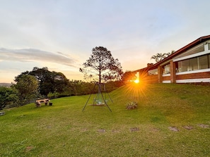 Um quintal gramado com balanço, um banco e uma casa com janelas grandes.