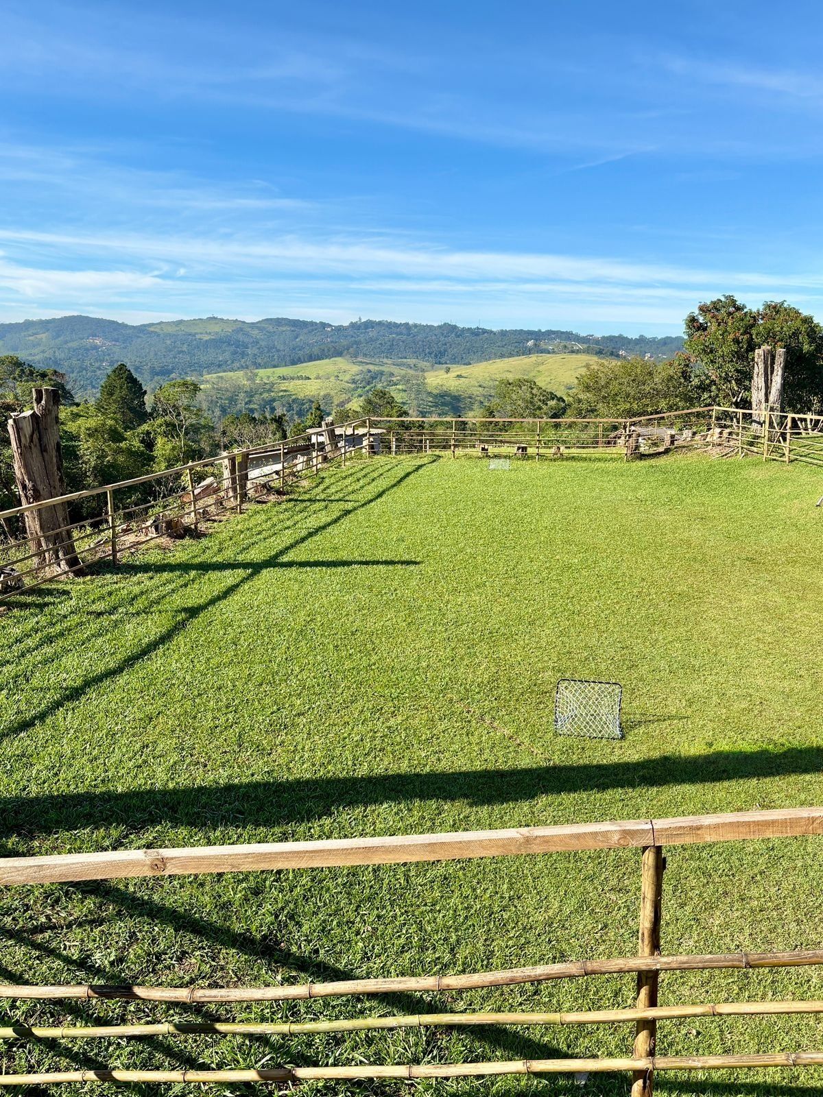 Un pastizal cercado con vistas despejadas a colinas distantes y un cielo azul.