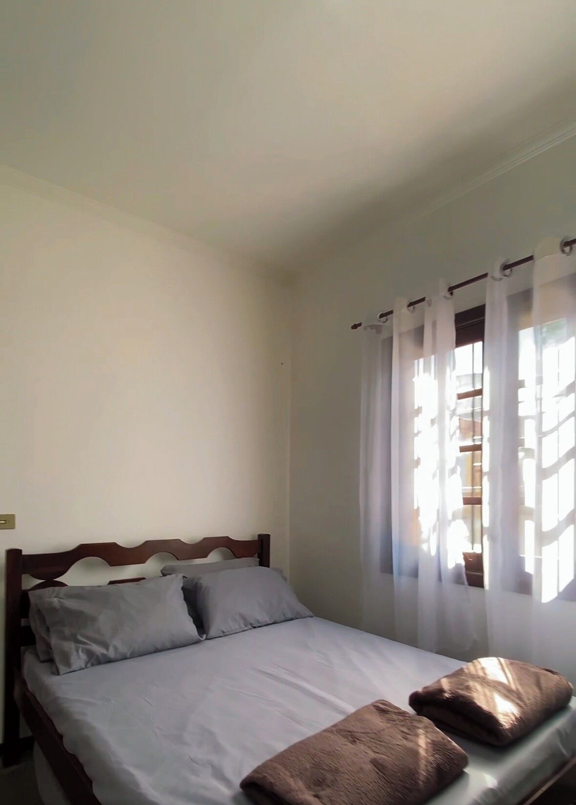 Una cama individual con cabecera de madera, ropa de cama blanca y dos almohadas marrones.