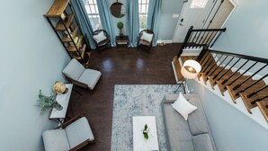 Un vaste espace de vie comprenant un canapé gris, deux fauteuils, une table basse et un escalier avec des rampes en bois.