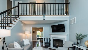 Un salon avec une cheminée, un téléviseur fixé au-dessus, un escalier et un coin repas.