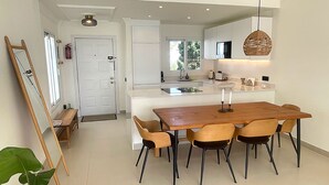 Une cuisine moderne dotée d’un îlot central, d’un coin repas avec une table et des chaises en bois, et d’un luminaire suspendu.