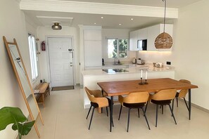 A modern kitchen with a central island, a dining area with a wooden table and chairs, and a hanging light fixture. - Beachfront apartment with sea views. (Estepona)