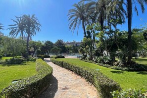 A stone pathway in a well-maintained garden with palm trees and neatly trimmed hedges. - Beachfront apartment with sea views. (Estepona)