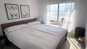 Une chambre dotée d’un grand lit, offrant une vue sur l’océan, et ornée de deux œuvres d’art florales encadrées au mur.