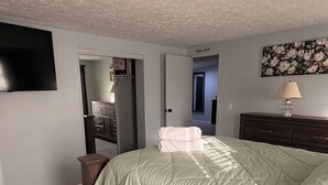 A bedroom with a bed, a dresser, a TV, and a door leading to another room.