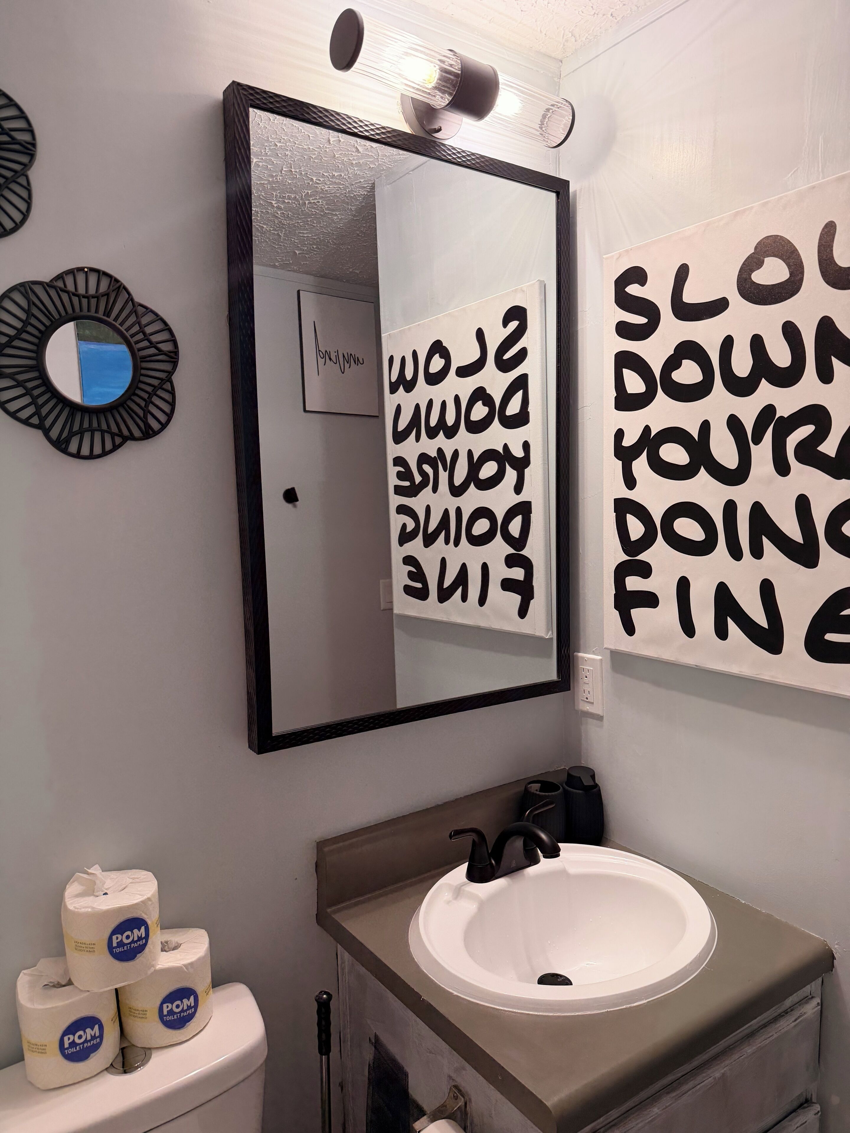Ein Badezimmer mit einem weißen Waschbecken, einem Spiegel und einer Wand mit motivierenden Texten.