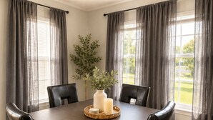 A dining room with a rectangular table, four chairs, a vase with a plant, and a candle on a tray.