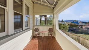 A covered porch with two chairs and a table, large windows, and a view of a residential area. - Spacious Stay in New Norfolk (New Norfolk)