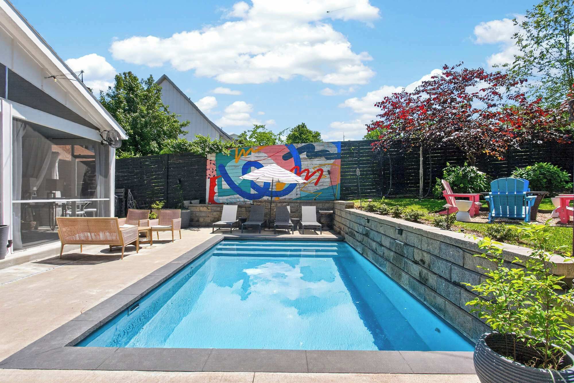 Une piscine avec des chaises longues, une fresque murale et un espace aménagé en jardin.