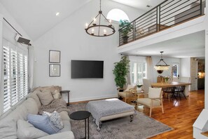 A spacious living area with a high ceiling, a dining table, and a staircase leading to an upper level. - Cozy Bungalow - Pool & Hot Tub 7 min to Broadway (Nashville)