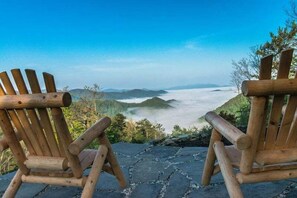 Two wooden Adirondack chairs facing a mountainous landscape with a view of the valley below. - Honeymoon Ridge- Luxury Mountaintop Cabin (Bryson City)