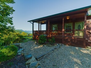 A wooden cabin with a covered porch, surrounded by a gravel driveway and greenery. - Honeymoon Ridge- Luxury Mountaintop Cabin (Bryson City)