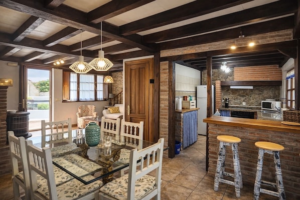 A rustic kitchen with exposed beams, a dining area with a glass table, and a bar with stools.