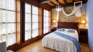 Ein Schlafzimmer mit einem großen Bett, Holzbalken, einer Steinwand und zwei Nachttischlampen.