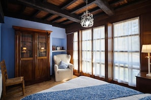 A room with a large bed, a wooden wardrobe, a chair, and a window with curtains.