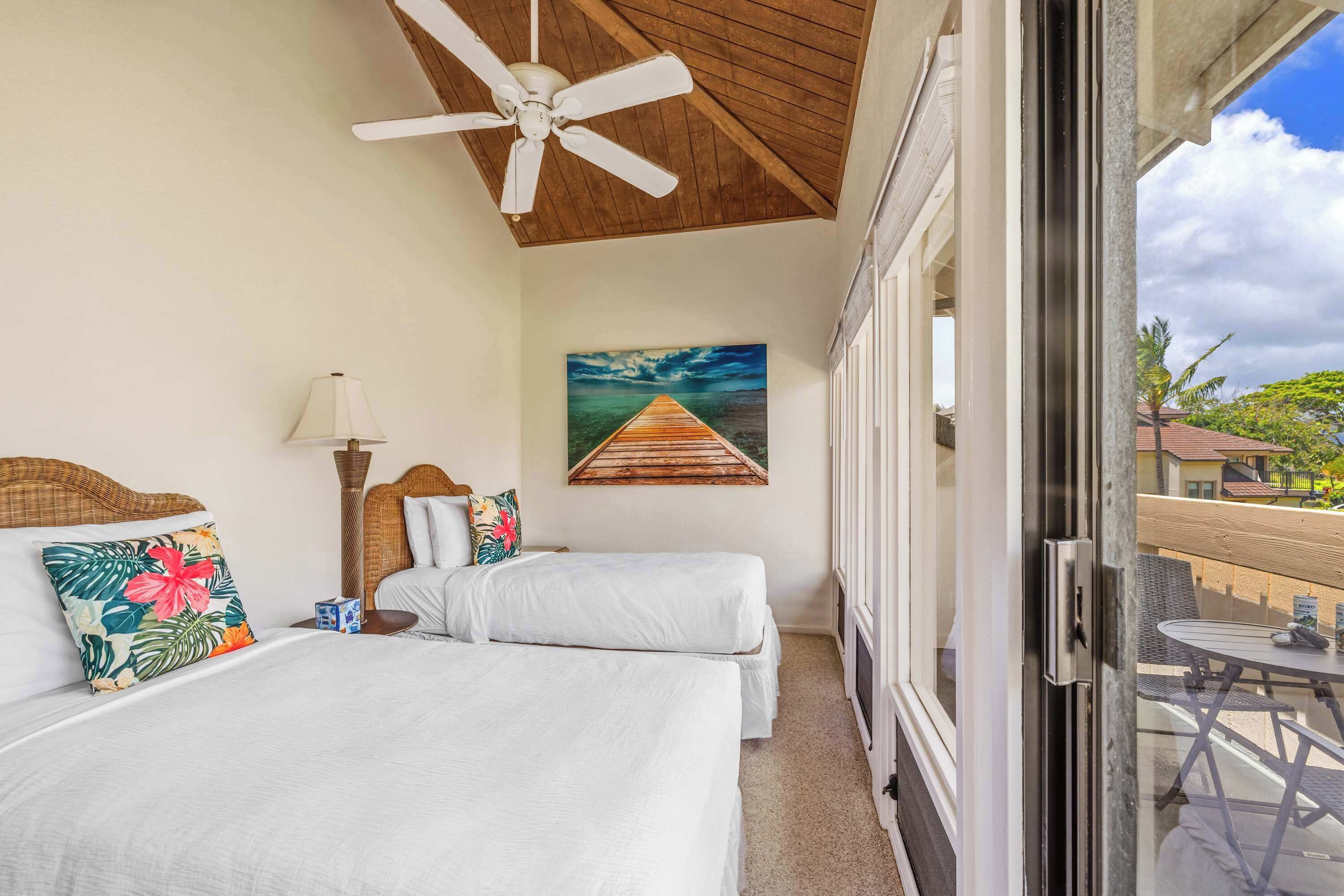 Habitación de hotel con dos camas, un ventilador de techo, un cuadro de un muelle y un balcón con vistas a los alrededores.