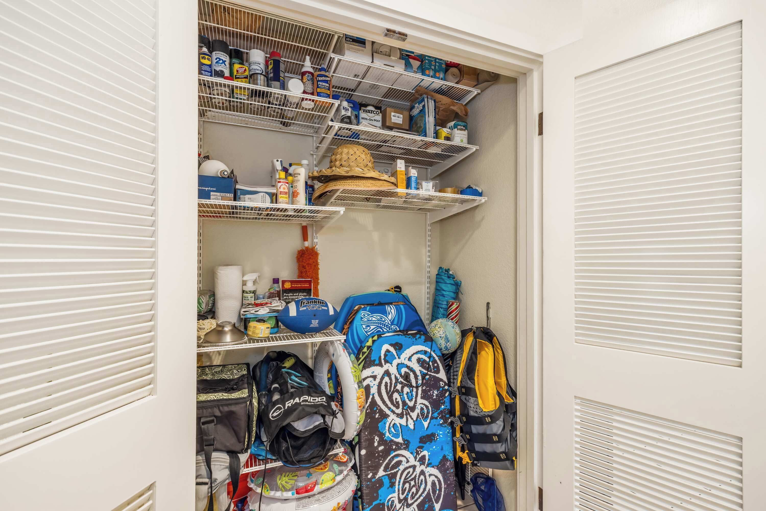 A storage closet with shelves containing cleaning supplies, a hat, and multiple backpacks.