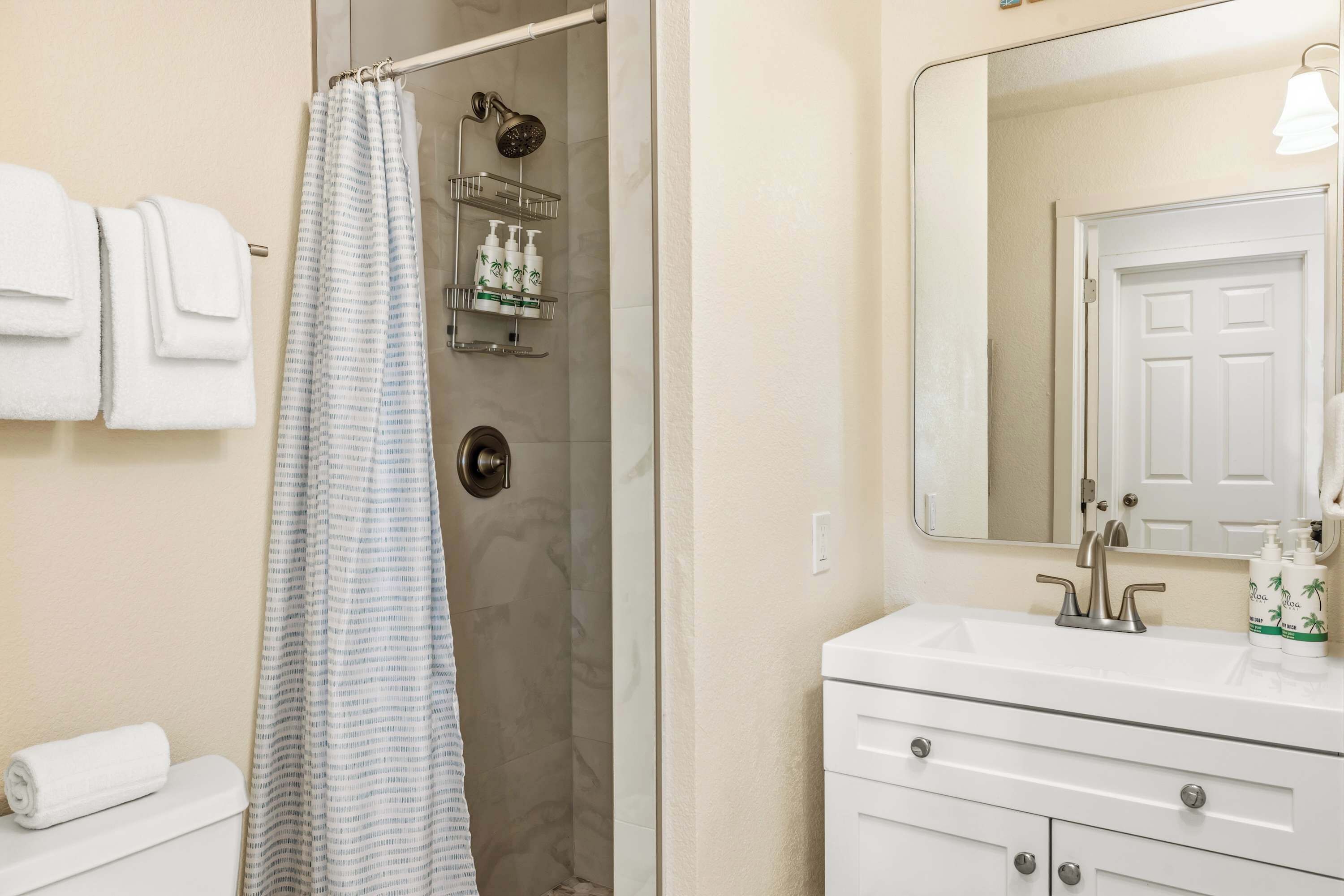 A bathroom with a shower, a toilet, a sink with a mirror, and a towel rack.
