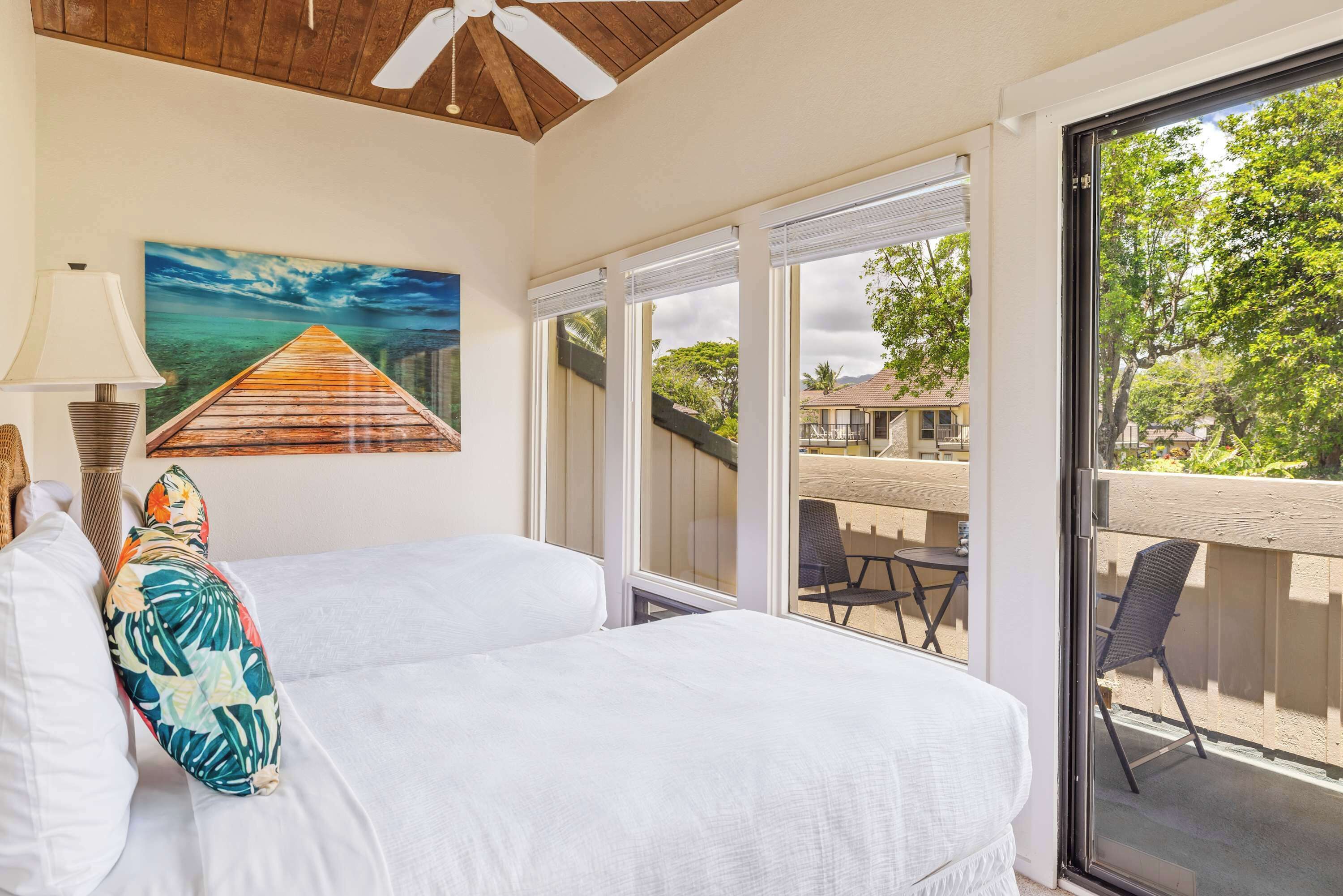 Hotelkamer met een bed, een schilderij van een houten pier, een balkon met tuinmeubilair en uitzicht op de omgeving.