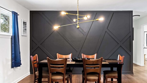A dining area with a black wall, wooden chairs, a black table, and a hanging light fixture. - Mins to Downtown! Chic & Modern - Elegant in Noir (Chattanooga)