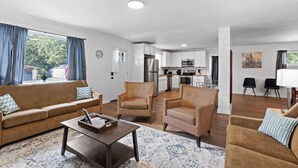 A living room with a sofa, armchairs, a coffee table, and a rug. There is a kitchen in the background with cabinets and appliances. - Mins to Downtown! Chic & Modern - Elegant in Noir (Chattanooga)