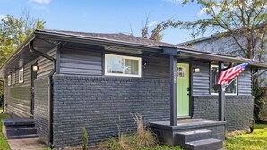 A small, single-story building with a green door, a small porch, and a flagpole with an American flag. - Mins to Downtown! Chic & Modern - Elegant in Noir (Chattanooga)