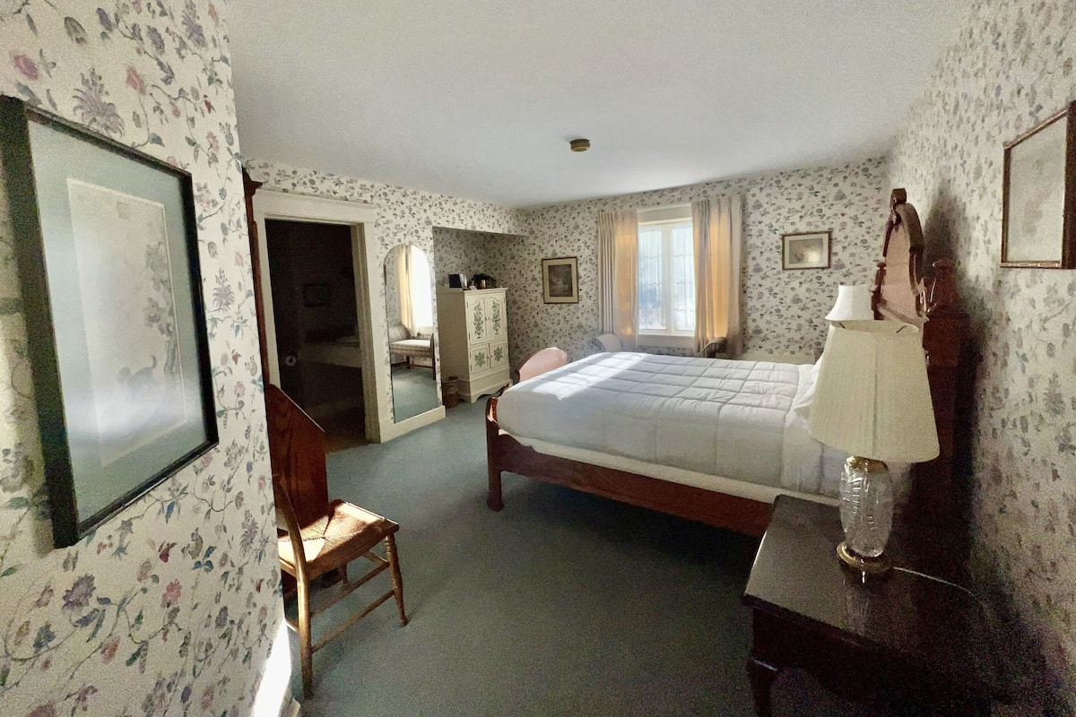 A hotel room with a bed, a chair, a dresser, a mirror, and a lamp.