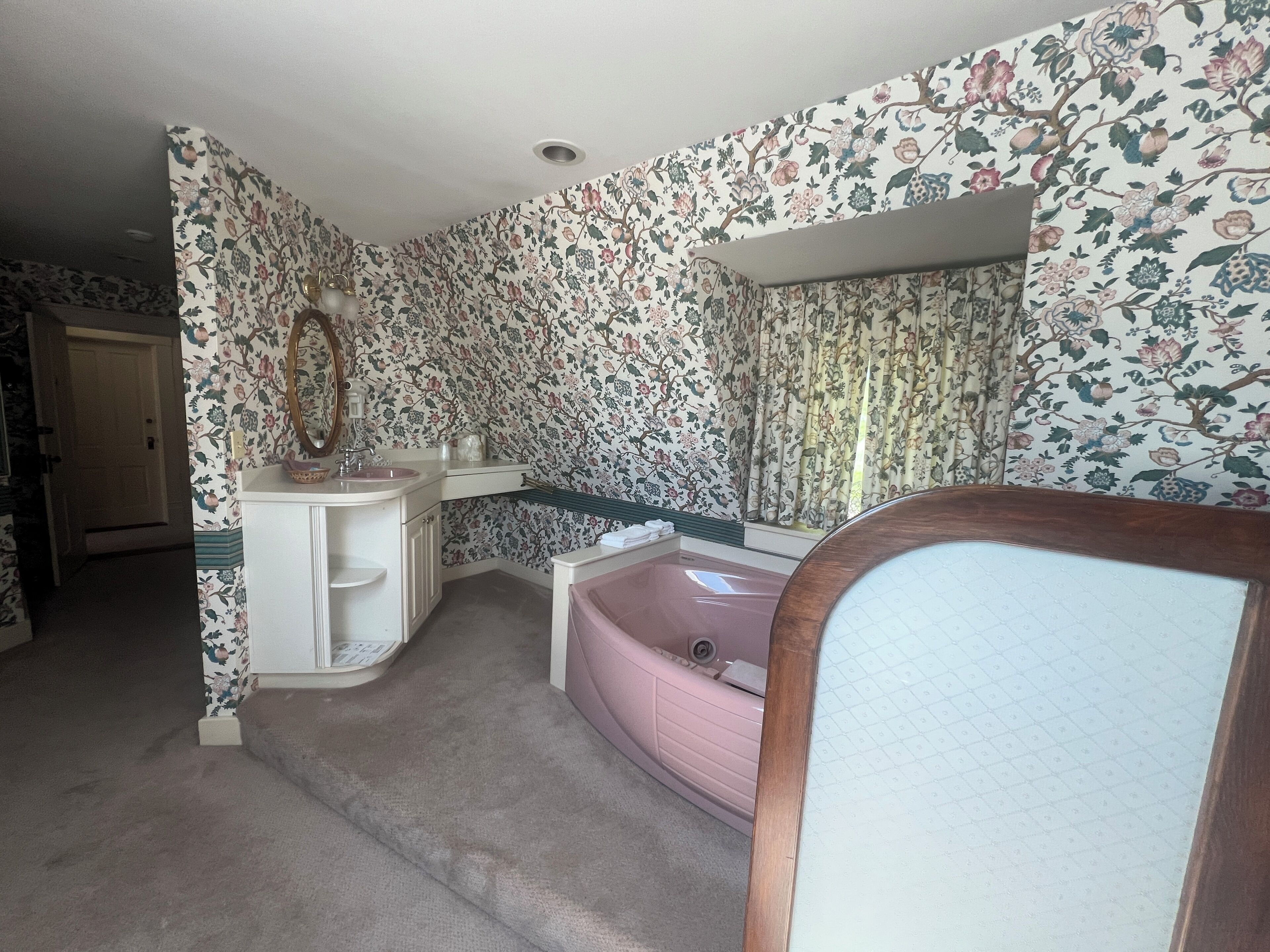 A bathroom with floral wallpaper, a sink, a mirror, a bathtub, and a shower area.
