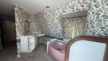 A bathroom with floral wallpaper, a sink, a mirror, a bathtub, and a shower area.