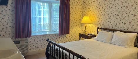 Een slaapkamer met een bed, een nachtkastje met lamp, een raam met gordijnen en een aan de muur bevestigde televisie.