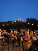 An outdoor seating area with tables and chairs, surrounded by trees and string lights.