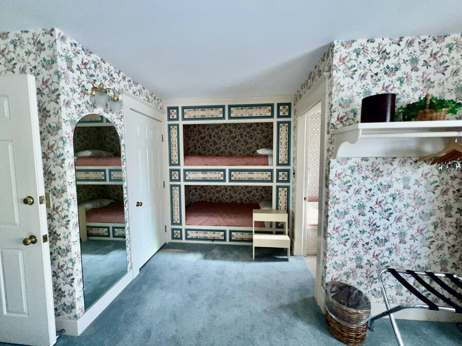 Una habitación con una cama litera, una mesita pequeña, una cesta y una estantería con una planta.