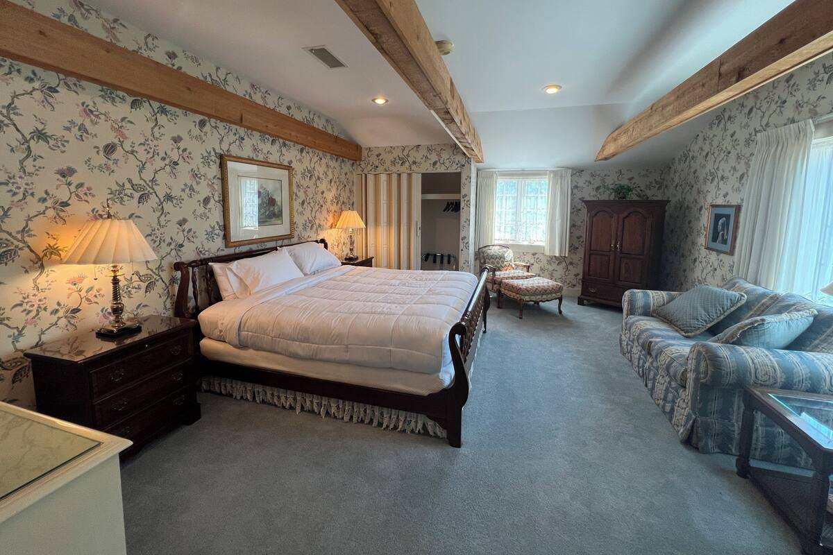 A bedroom with a large bed, a chair, a cabinet, and a dresser.
