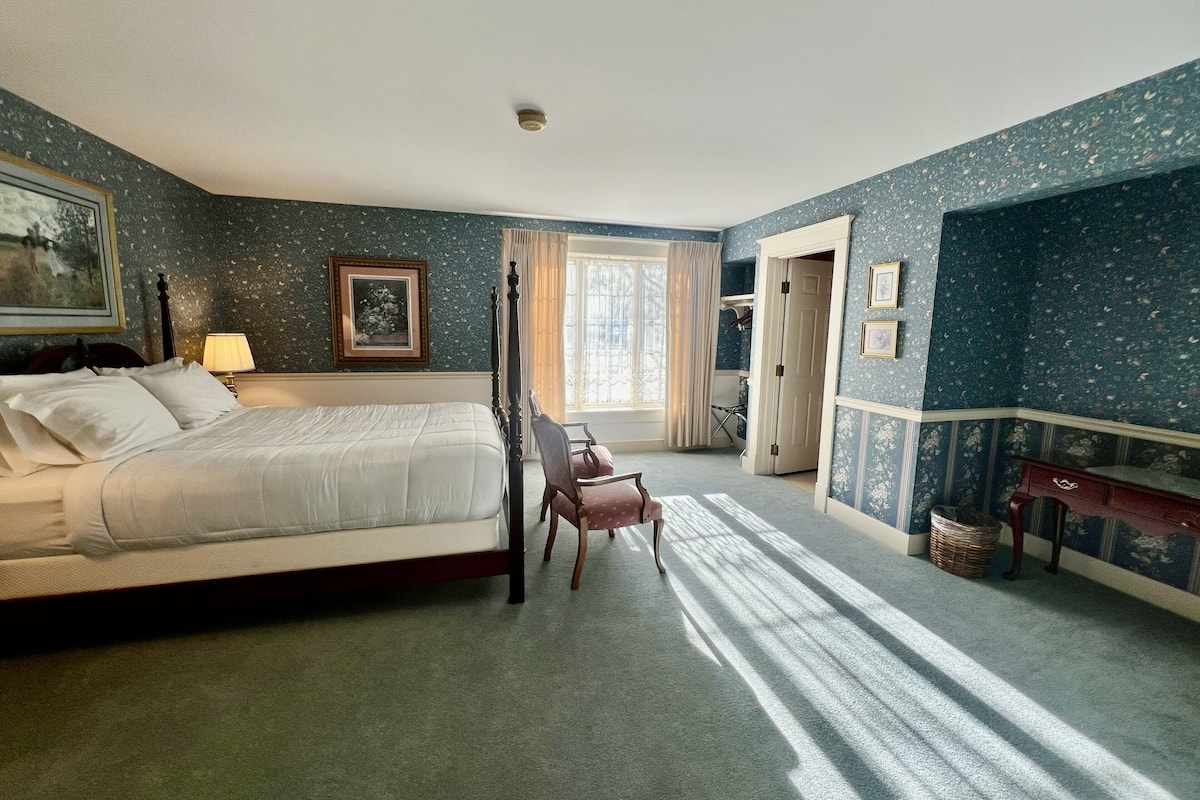 A bedroom with a bed, a chair, a desk, a window, and a door.