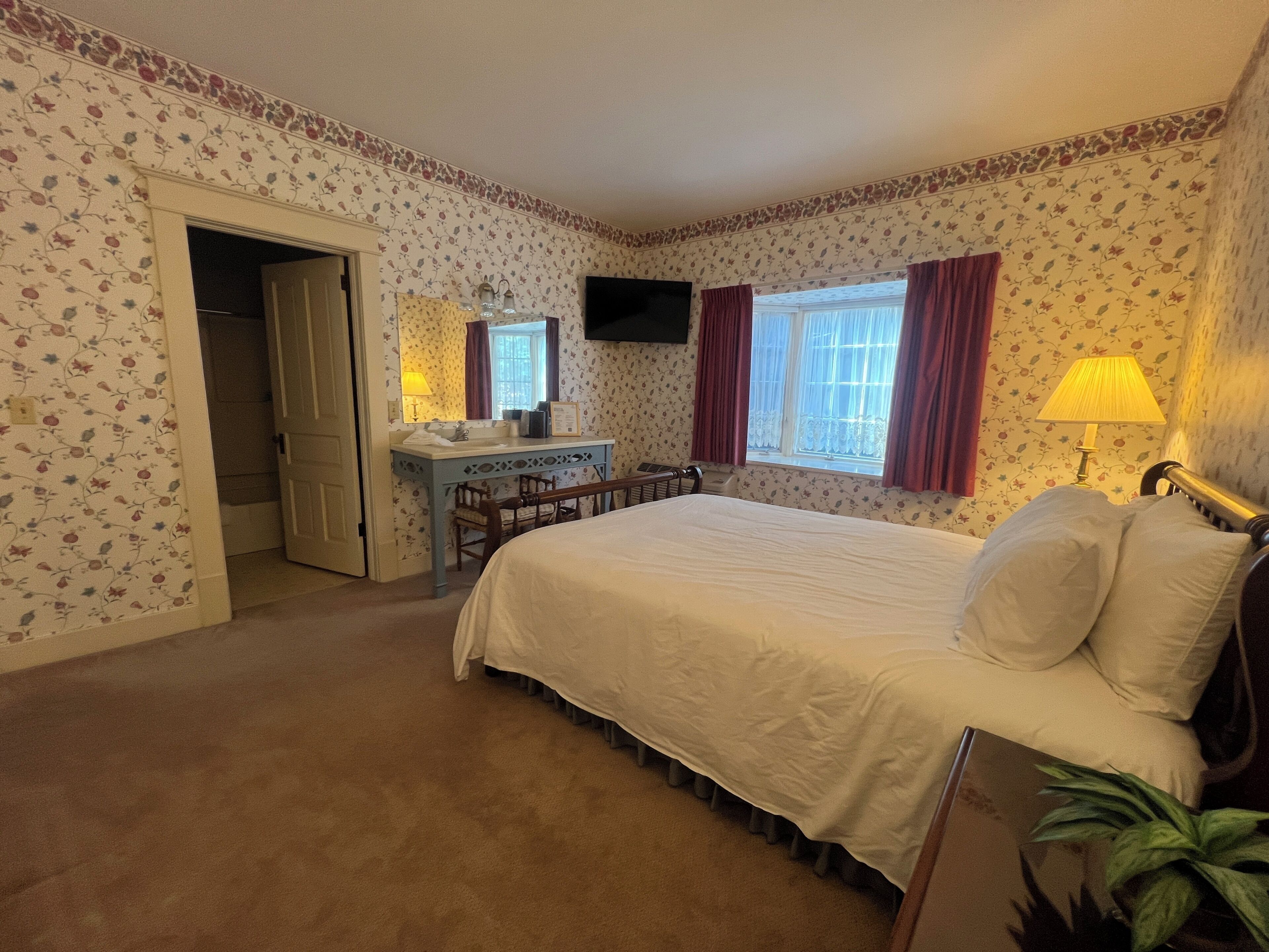 A bedroom with a bed, a desk, a chair, a television, and a window with curtains.