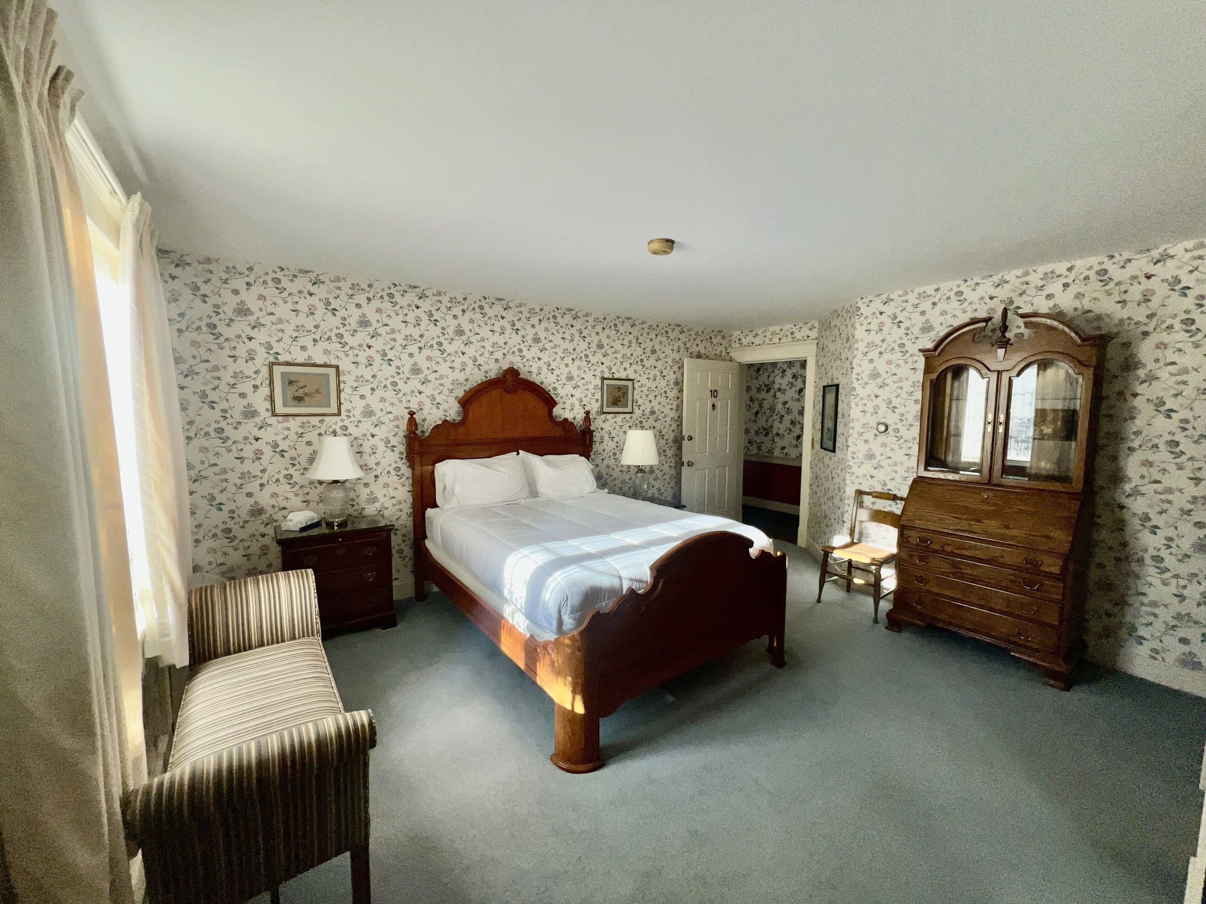 Ein Schlafzimmer mit einem hölzernen Bett, einem Schminktisch, einem Stuhl und einer Tür zu einem weiteren Raum.
