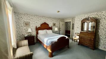 Ein Schlafzimmer mit einem hölzernen Bett, einem Schminktisch, einem Stuhl und einer Tür zu einem weiteren Raum.