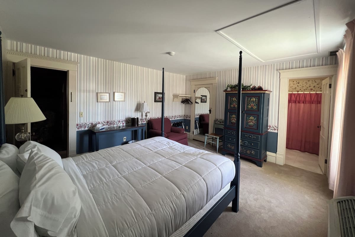 A bedroom with a four-poster bed, a dresser, a chair, and a desk with a lamp.