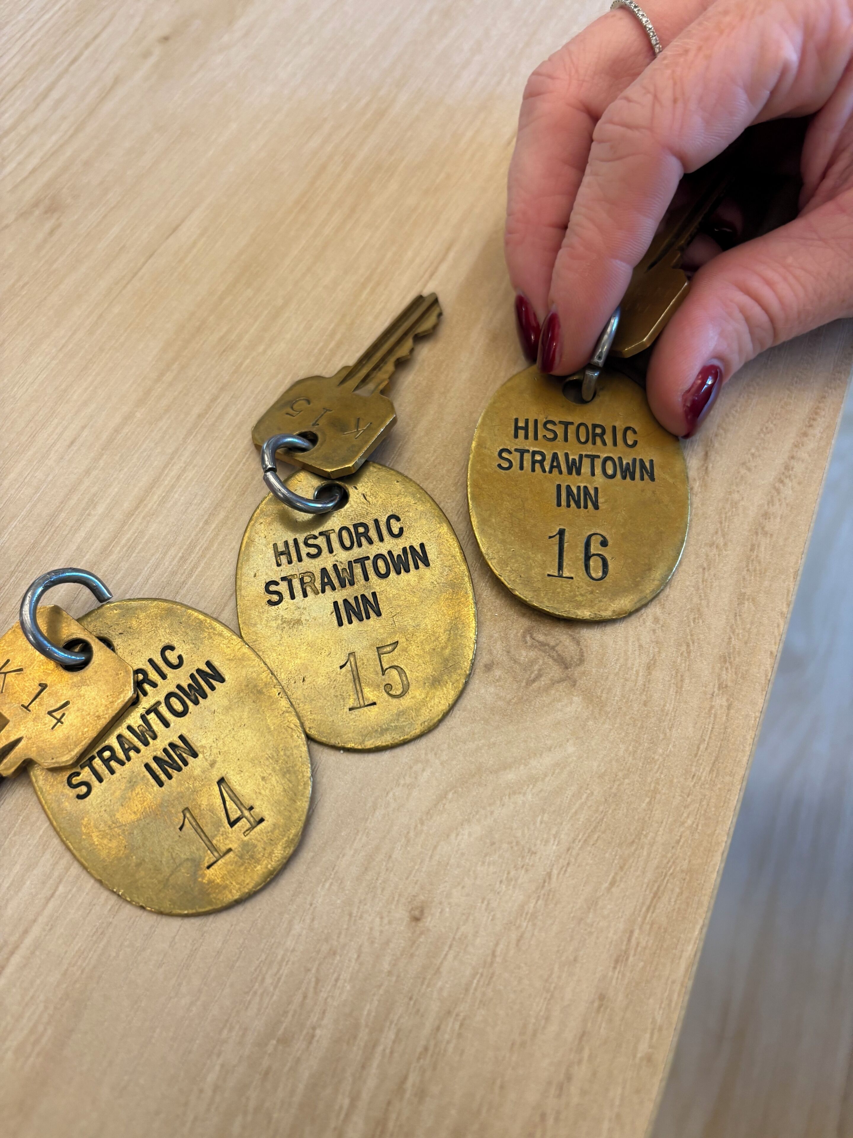Tres etiquetas metálicas de bronce con inscripciones y números, sobre una superficie de madera.