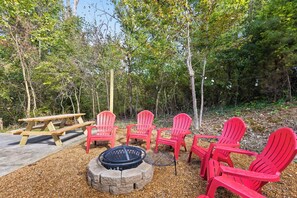 A fire pit surrounded by red chairs and a picnic table in a wooded area. - Mins to Downtown! Deck & Firepit - Elmwood Retreat (Chattanooga)