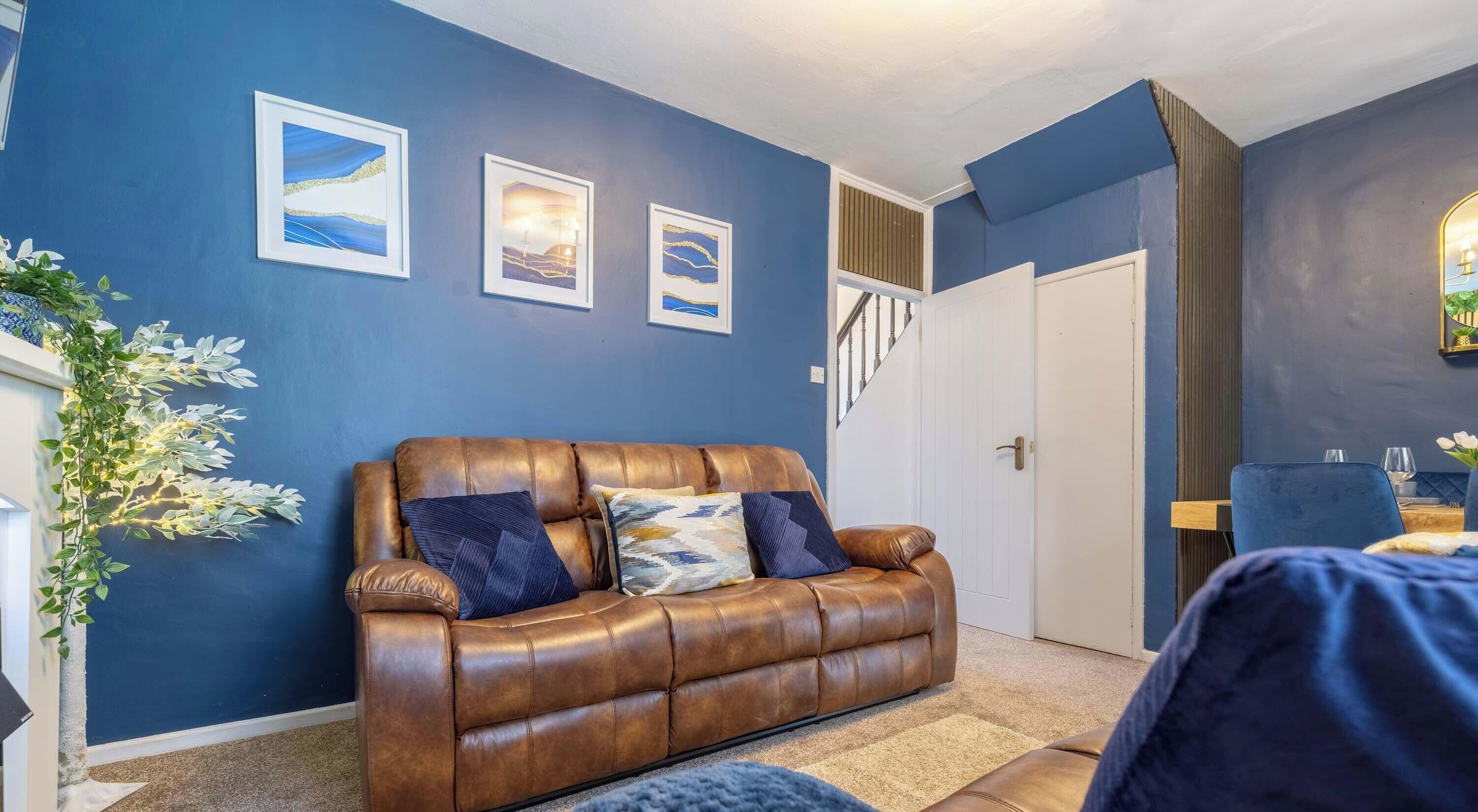 A room with a brown leather sofa, a staircase, and framed artwork on the wall.