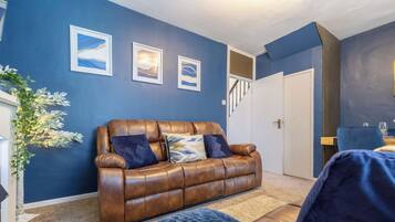 A room with a brown leather sofa, a staircase, and framed artwork on the wall.