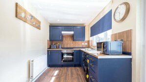 A compact kitchen with dark blue cabinets, a built-in oven, a microwave, and a clock on the wall.