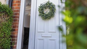A white door with a wreath, a brick wall, and a window with frosted glass.