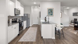 A modern kitchen with white cabinets, stainless appliances, and a central island with bar stools. - Modern Farmhouse Retreat w Patio & Yard (Lockhart)