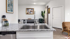 A modern kitchen with a granite countertop, stainless steel sink, and a dishwasher. - Modern Farmhouse Retreat w Patio & Yard (Lockhart)