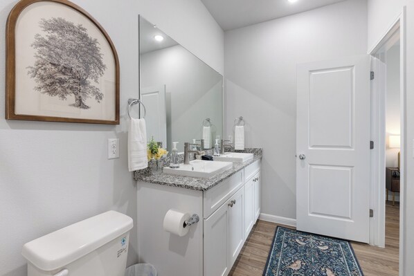 A bathroom with a toilet, two sinks, a mirror, and a door.