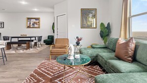 A modern living room with a dining area, green sofa, and artwork on the walls. - Modern Farmhouse Retreat w Patio & Yard (Lockhart)